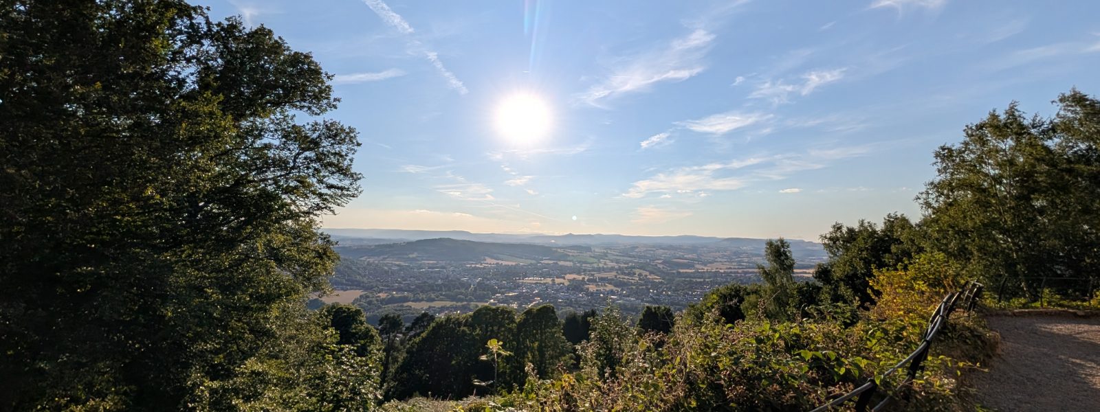 looking out over the valley from the top of a hill, sun high, path curving off to the right
