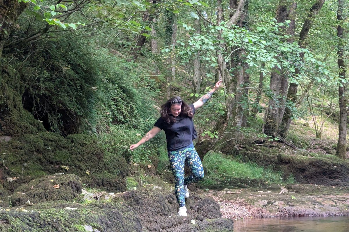 me hopping between mossy rocks beside a river in a wood, arms out for balance